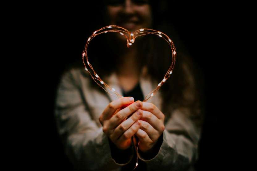 Coeur Silhouette d'une femme dans la pénombre avec une veste grise qui tient devant elle un cœur fait en guirlande lumineuse